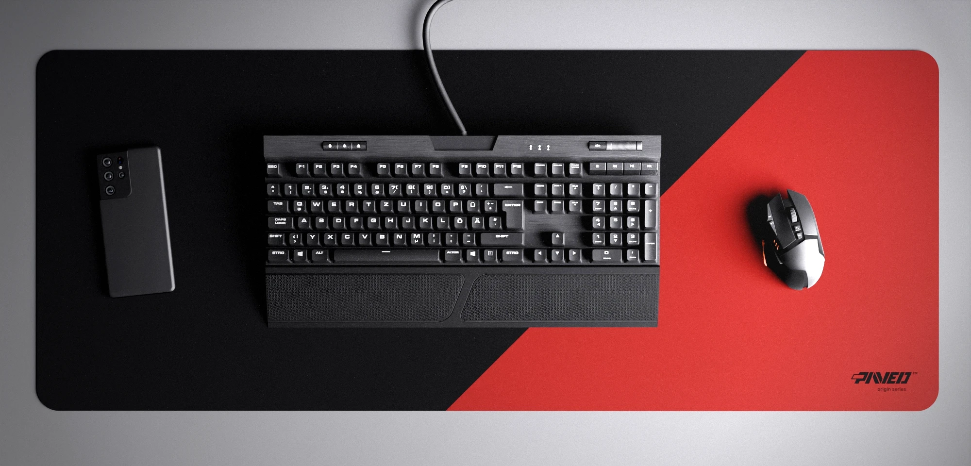 Top view of Imperial Edge Runner XXL deskmat 1000mm x 400mm right-handed variant with minimalistic diagonal split design in red and black, hydrophobic easy-to-clean antimicrobial surface, shown with full-size mechanical keyboard, gaming mouse, and smartphone for scale, 600% lighter non-slip base with no rubbery smell, durable stitch-free edges.