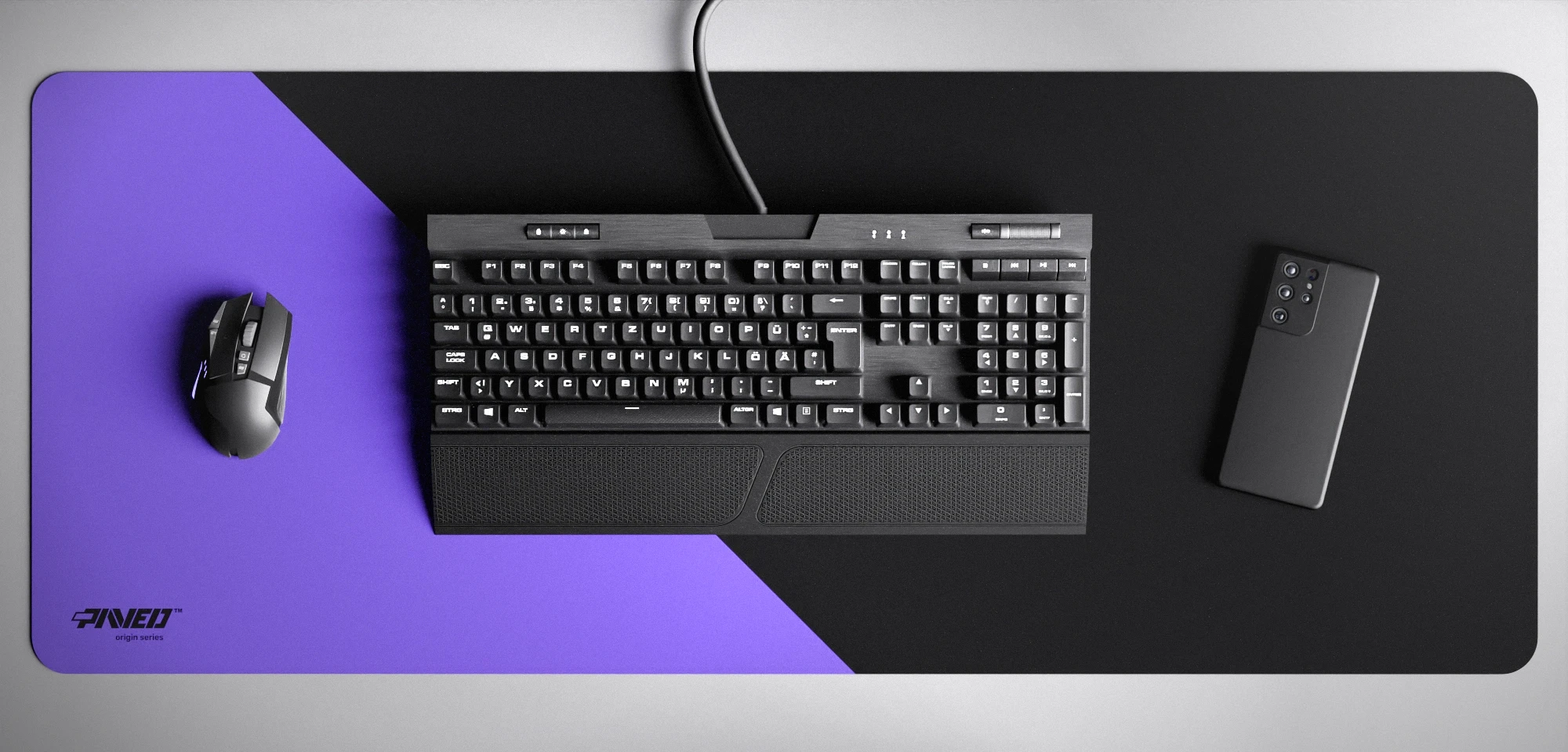 Top view of Amethyst Edge Runner XXL deskmat 1000mm x 400mm left-handed variant featuring diagonal split design in purple and black, water-resistant antimicrobial polyester surface, shown with full-size mechanical keyboard, gaming mouse, and smartphone for scale, ultra-lightweight odour-free AreoFlex microruber base, stitch-free professional finish.