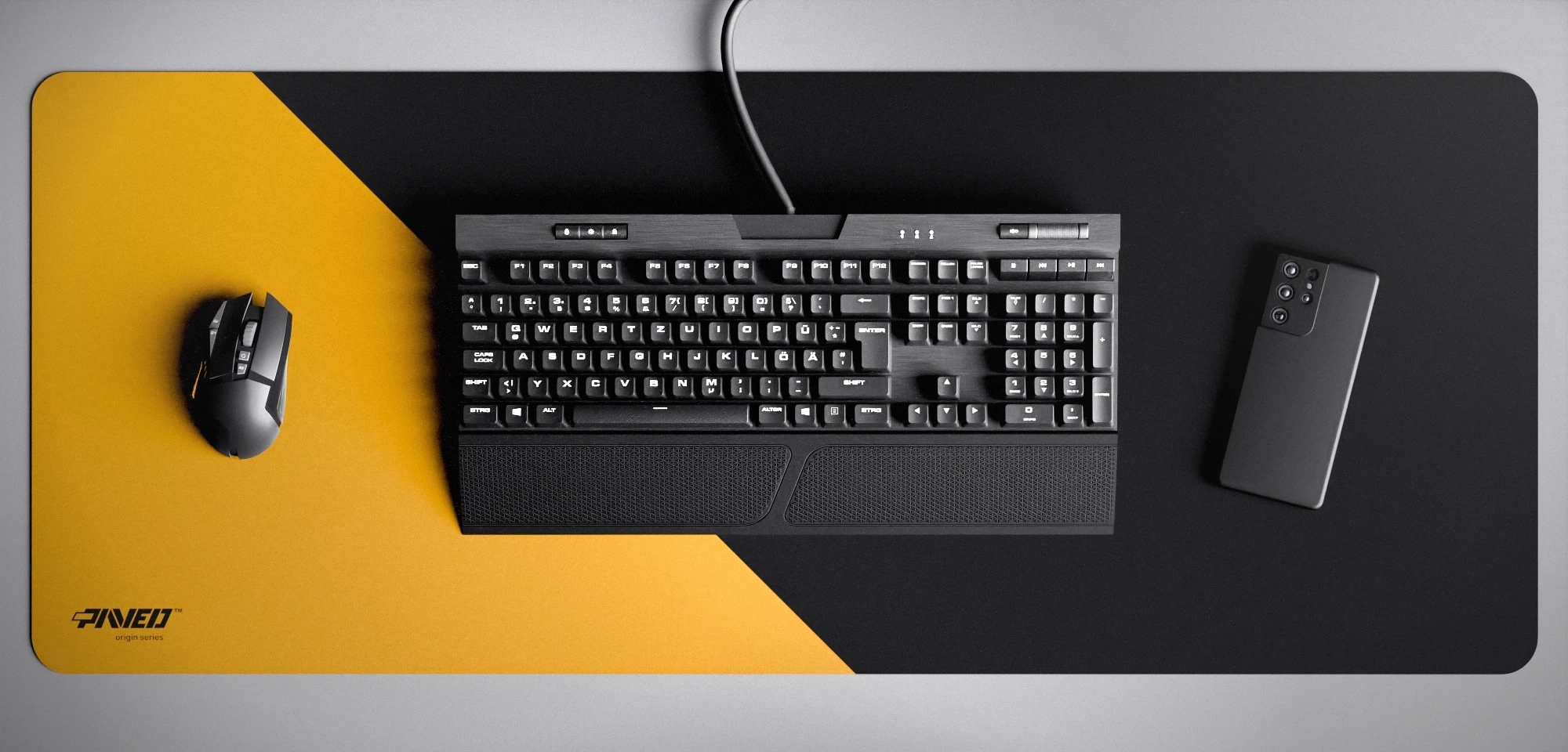 Top view of Desert Edge Runner XXL deskmat 1000mm x 400mm left-handed variant featuring diagonal split design in deep yellow and black, water-resistant antimicrobial polyester surface, shown with full-size mechanical keyboard, gaming mouse, and smartphone for scale, ultra-lightweight odour-free AreoFlex microruber base, stitch-free professional finish.