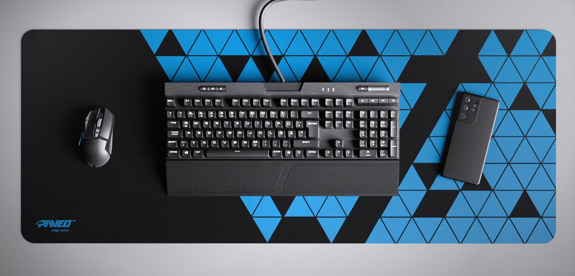 Top view of Night Sky Prism XXL deskmat 1000mm x 400mm left-handed variant featuring abstract geometric triangular pattern in sky blue and black, water-resistant antimicrobial polyester surface, shown with full-size mechanical keyboard, gaming mouse, and smartphone for scale, ultra-lightweight odour-free AreoFlex microruber base, stitch-free professional finish.