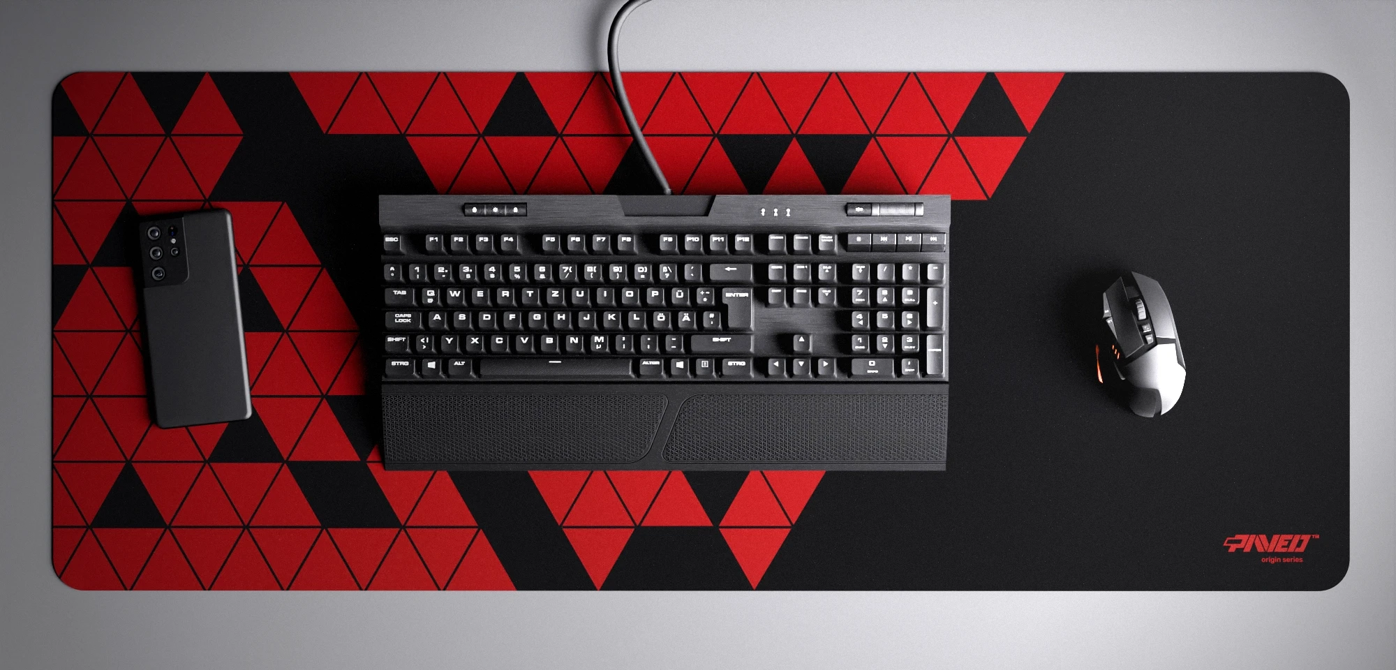 Top view of Night Imperial Prism XXL deskmat 1000mm x 400mm right-handed variant with minimalistic geometric triangular prism pattern in red and black, hydrophobic easy-to-clean antimicrobial surface, shown with full-size mechanical keyboard, gaming mouse, and smartphone for scale, 600% lighter non-slip base with no rubbery smell, durable stitch-free edges.