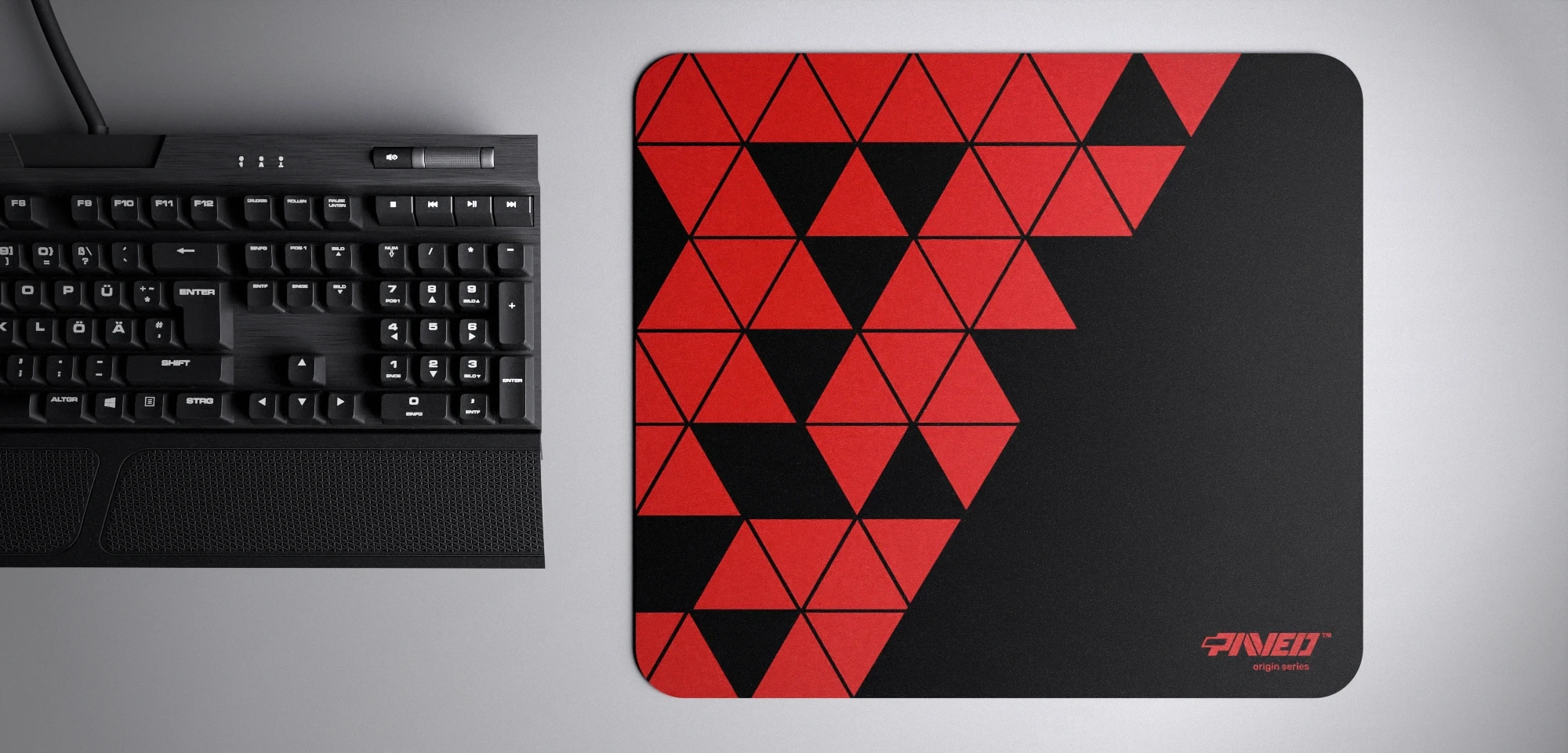 Top view of Night Imperial Prism M size mousepad 360mm x 320mm right-handed variant with geometric red and black triangular pattern, hydrophobic easy-to-clean surface with antimicrobial properties, shown with full-size mechanical keyboard for scale, 600% lighter with no rubbery odour base, durable stitch-free finish.