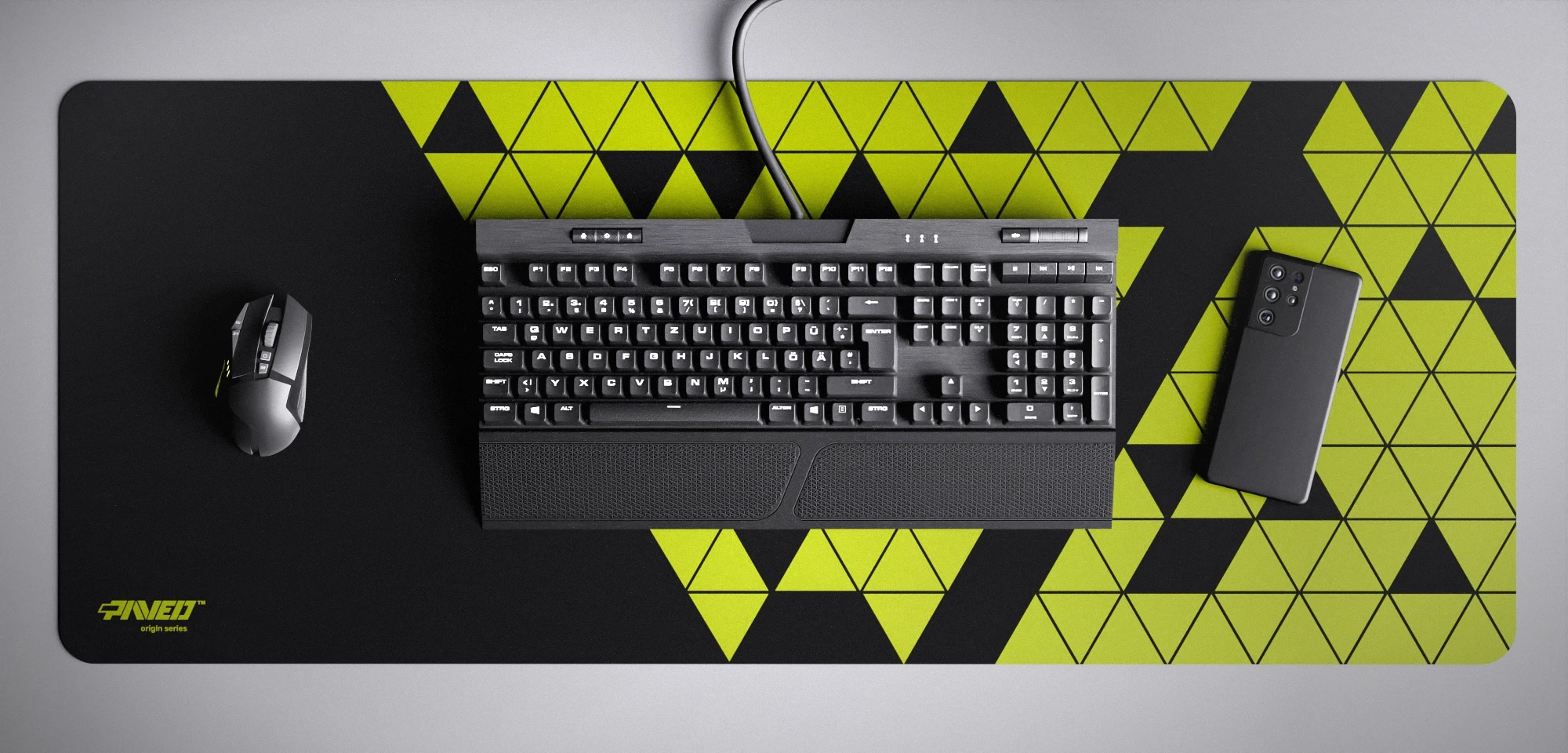 Top view of Night Toxic Prism XXL deskmat 1000mm x 400mm left-handed variant featuring abstract geometric triangular pattern in light green and black, water-resistant antimicrobial polyester surface, shown with full-size mechanical keyboard, gaming mouse, and smartphone for scale, ultra-lightweight odour-free AreoFlex microruber base, stitch-free professional finish.