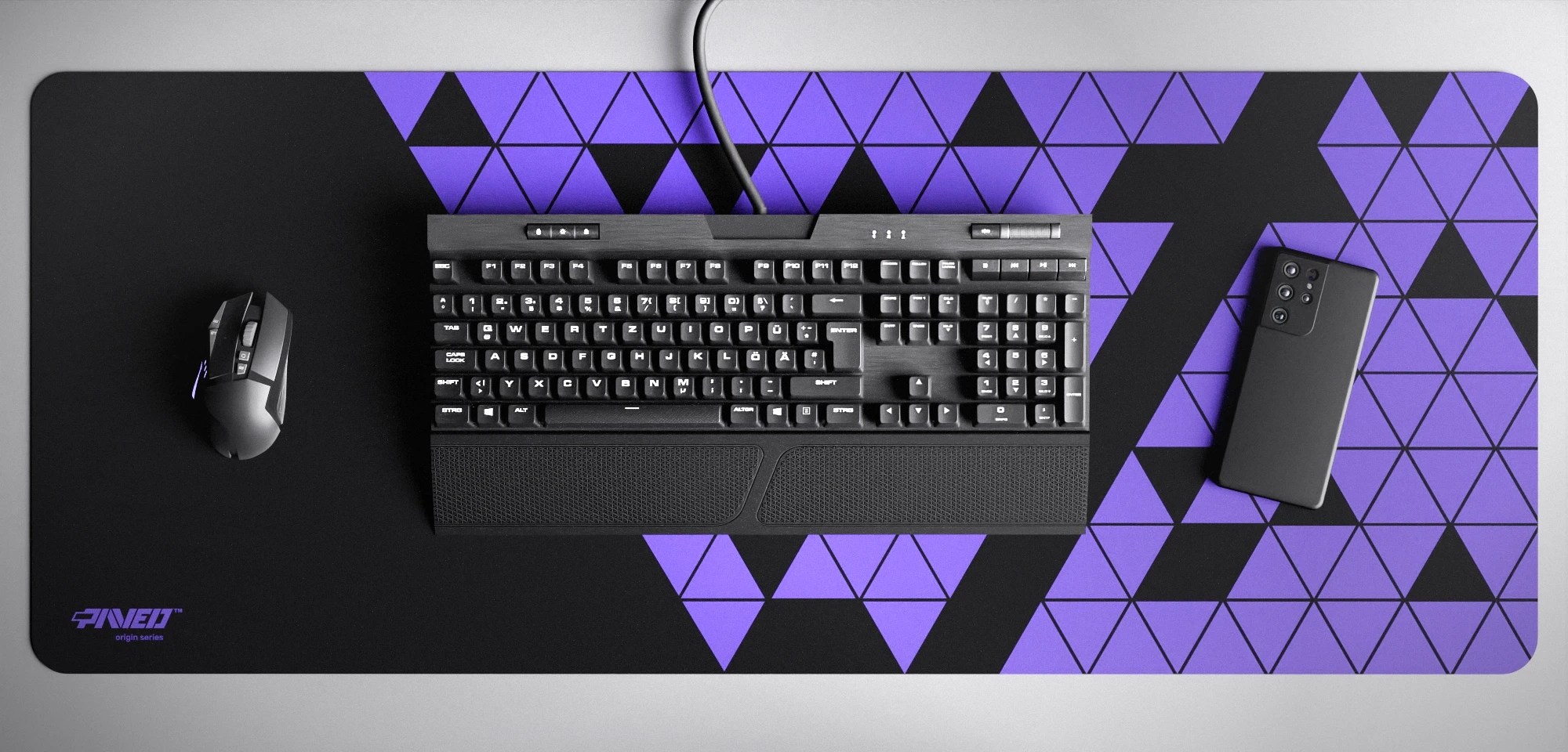 Top view of Night Amethyst Prism XXL deskmat 1000mm x 400mm left-handed variant featuring abstract geometric triangular pattern in purple and black, water-resistant antimicrobial polyester surface, shown with full-size mechanical keyboard, gaming mouse, and smartphone for scale, ultra-lightweight odour-free AreoFlex microruber base, stitch-free professional finish.