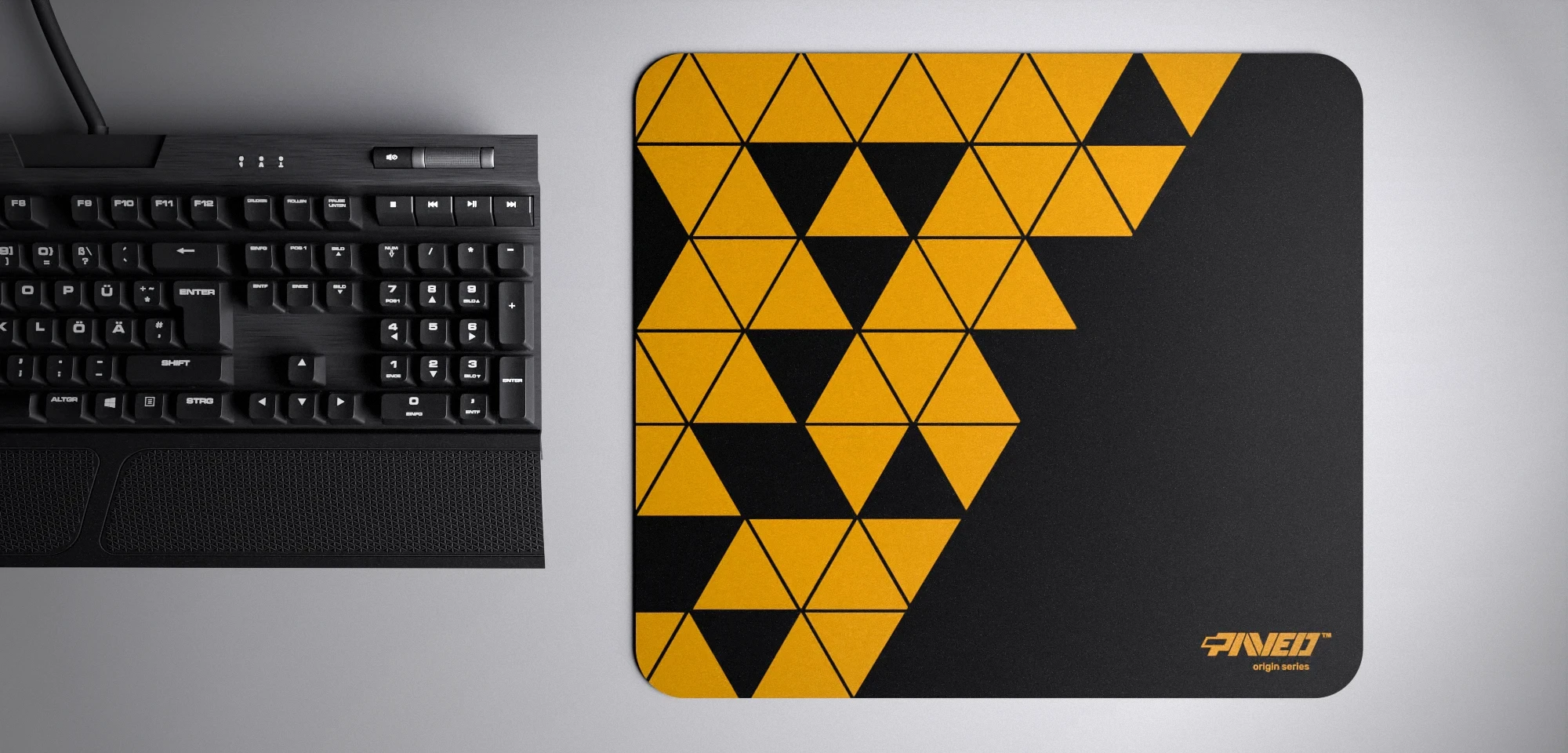 Top view of Night Desert Prism M size mousepad 360mm x 320mm right-handed variant with geometric deep yellow and black triangular pattern, hydrophobic easy-to-clean surface with antimicrobial properties, shown with full-size mechanical keyboard for scale, 600% lighter with no rubbery odour base, durable stitch-free finish.