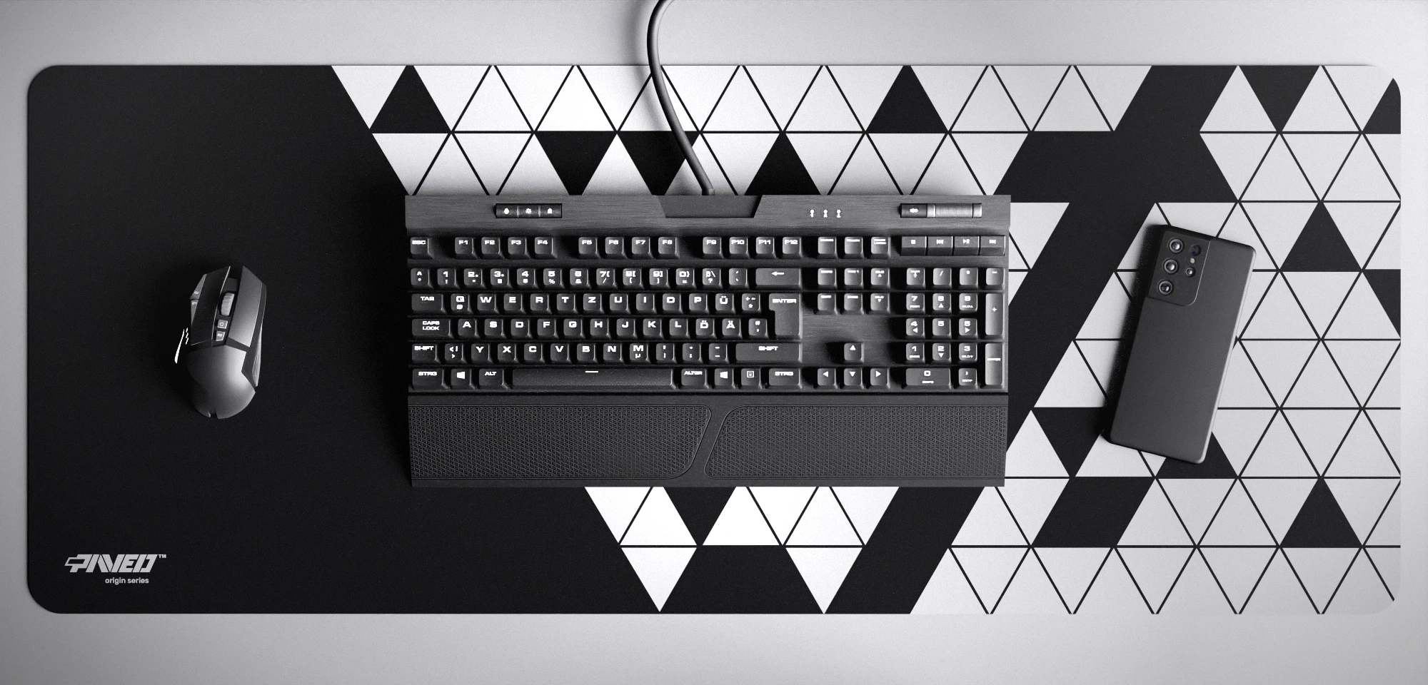 Top view of Night Prism XXL deskmat 1000mm x 400mm left-handed variant featuring abstract geometric triangular pattern in white and black, water-resistant antimicrobial polyester surface, shown with full-size mechanical keyboard, gaming mouse, and smartphone for scale, ultra-lightweight odour-free AreoFlex microruber base, stitch-free professional finish.