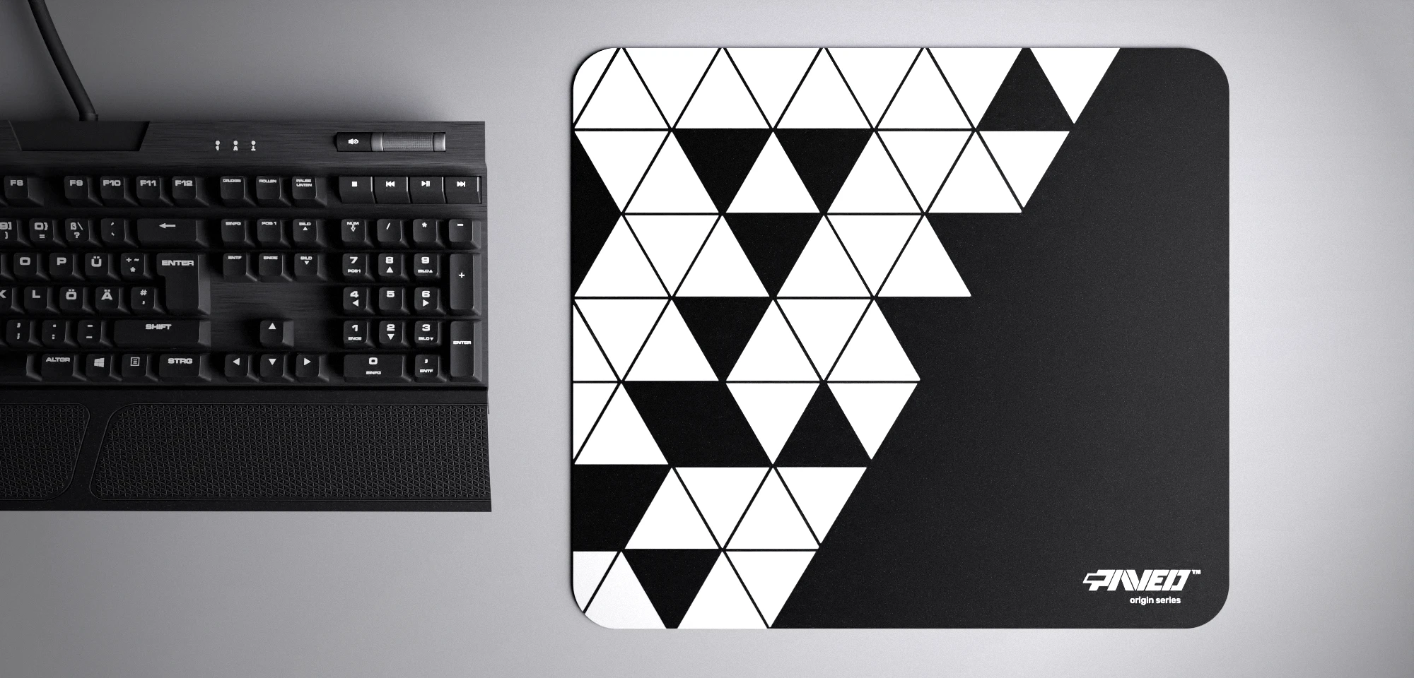 Top view of Night Prism M size mousepad 360mm x 320mm right-handed variant with geometric white and black triangular pattern, hydrophobic easy-to-clean surface with antimicrobial properties, shown with full-size mechanical keyboard for scale, 600% lighter with no rubbery odour base, durable stitch-free finish.