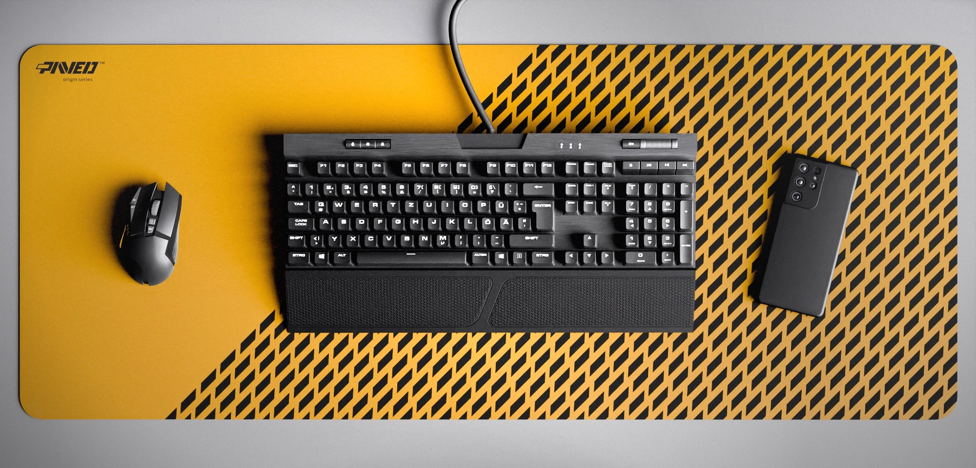 Top view of Desert Panther XXL deskmat 1000mm x 400mm left-handed variant featuring diagonal split design with geometric panther spot pattern in deep yellow and black, water-resistant antimicrobial polyester surface, shown with full-size mechanical keyboard, gaming mouse, and smartphone for scale, ultra-lightweight odour-free AreoFlex microruber base, stitch-free professional finish.