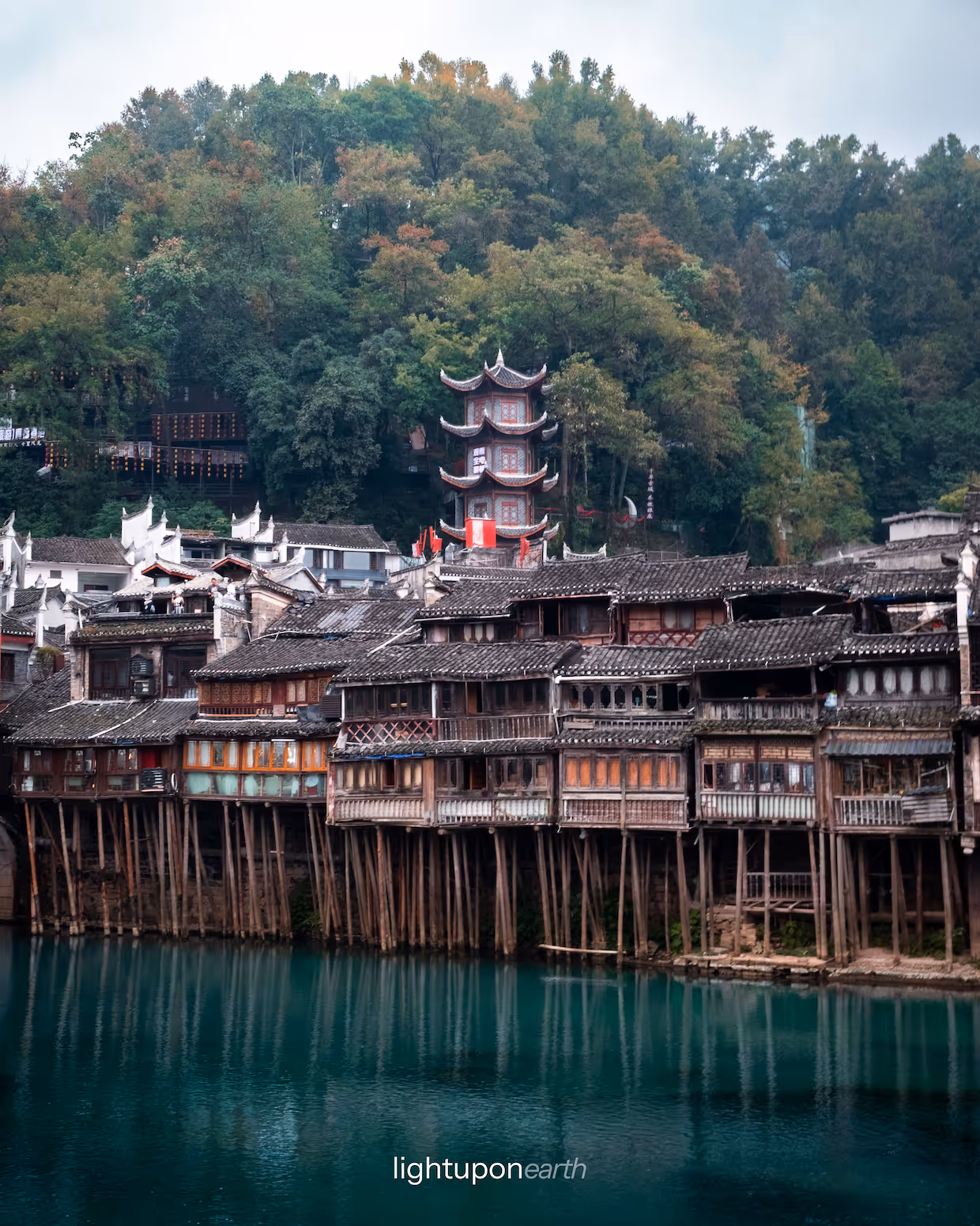 wooden houses on the riverbank with a temple in the background