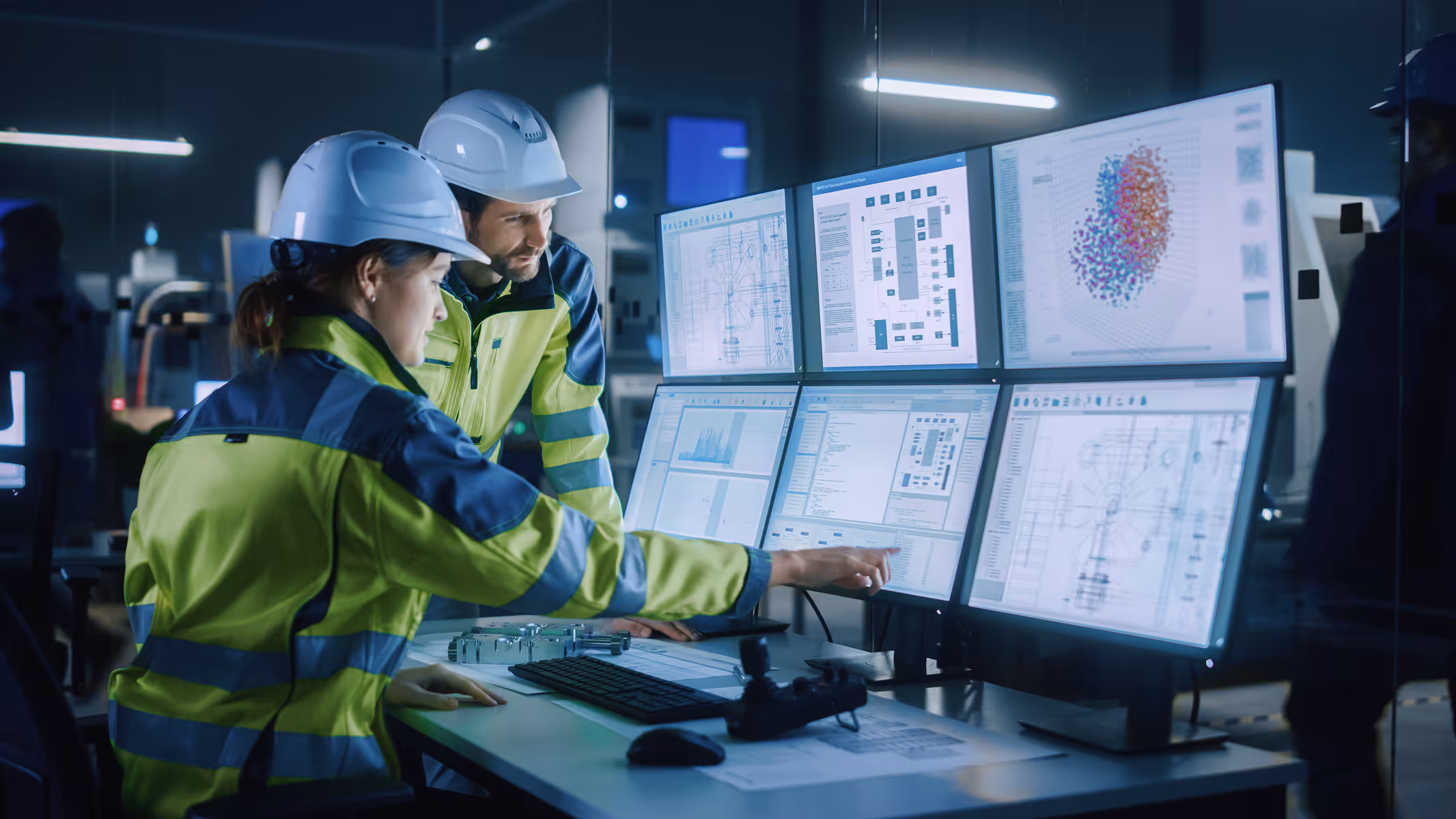 Two engineers in safety helmets and high-visibility jackets analyzing data on multiple computer monitors.
