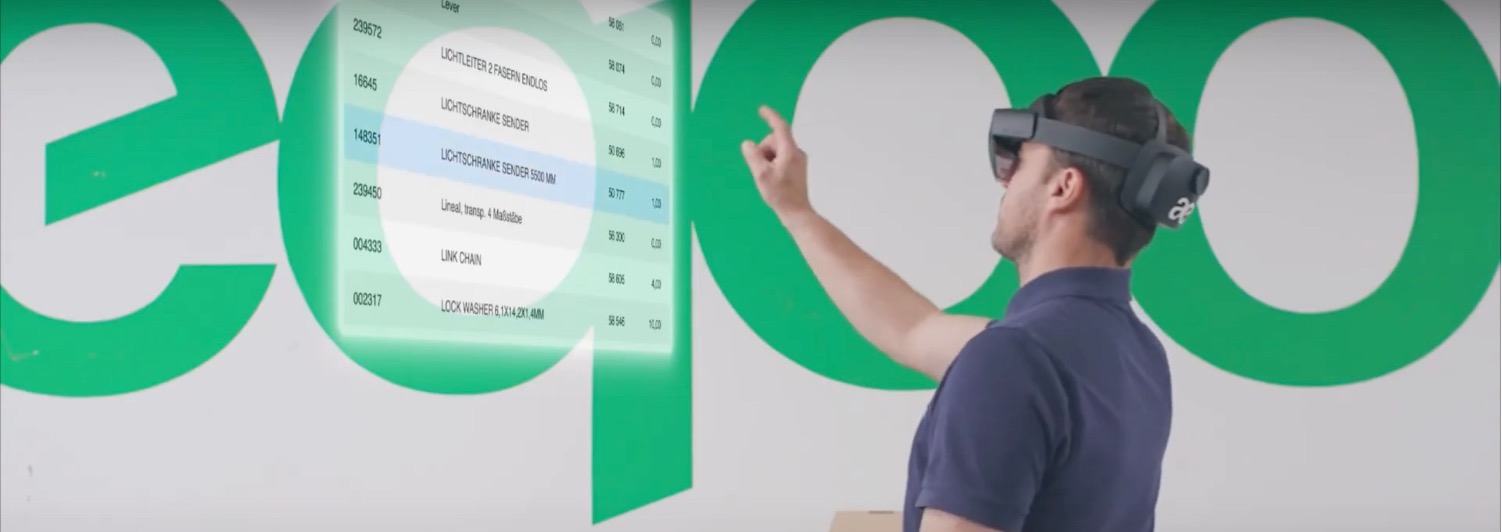 Man wearing augmented reality headset interacts with a floating digital interface displaying a list of items.