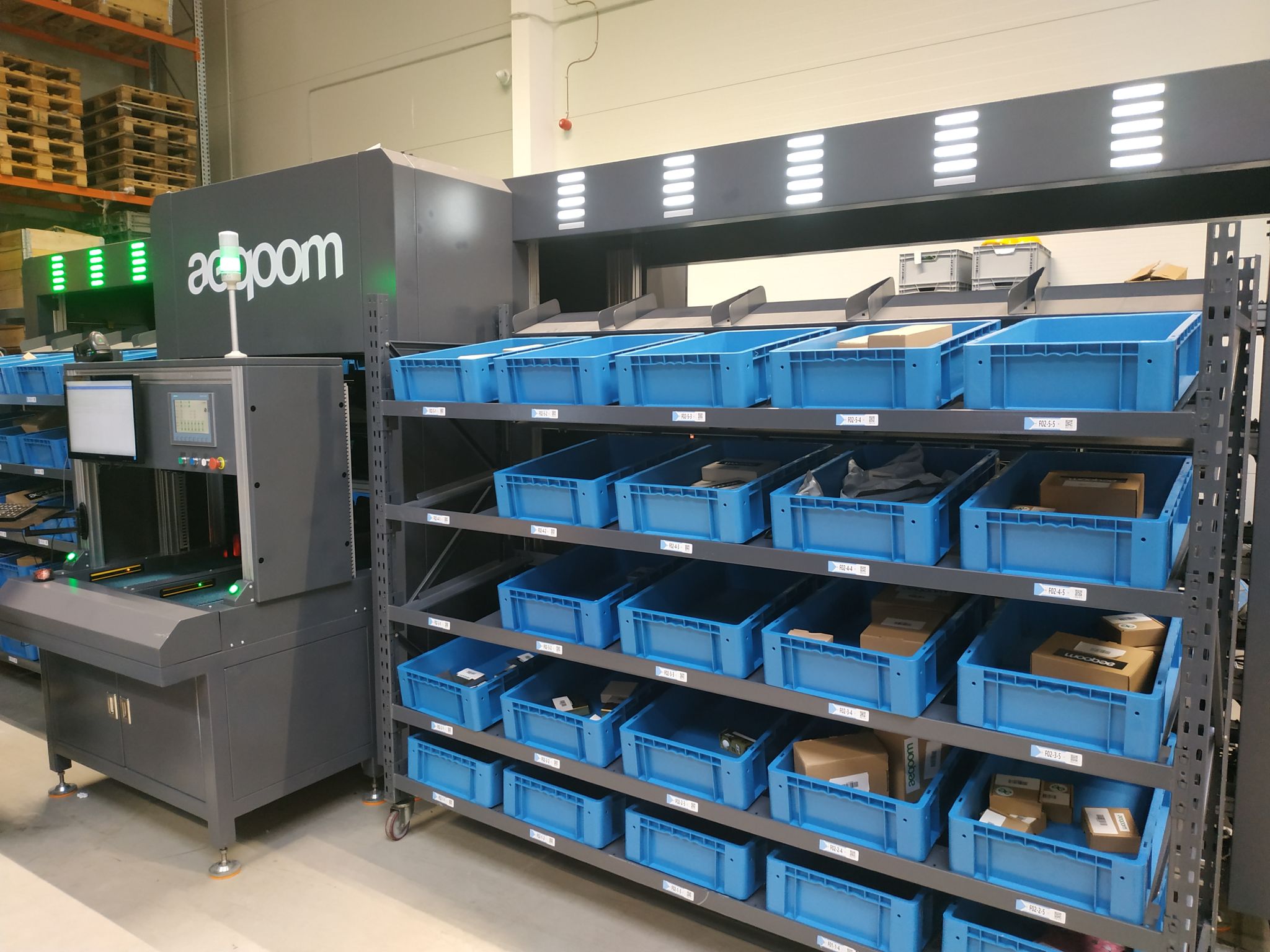 Industrial automated sorting machine with blue bins containing packages and products in a warehouse setting.