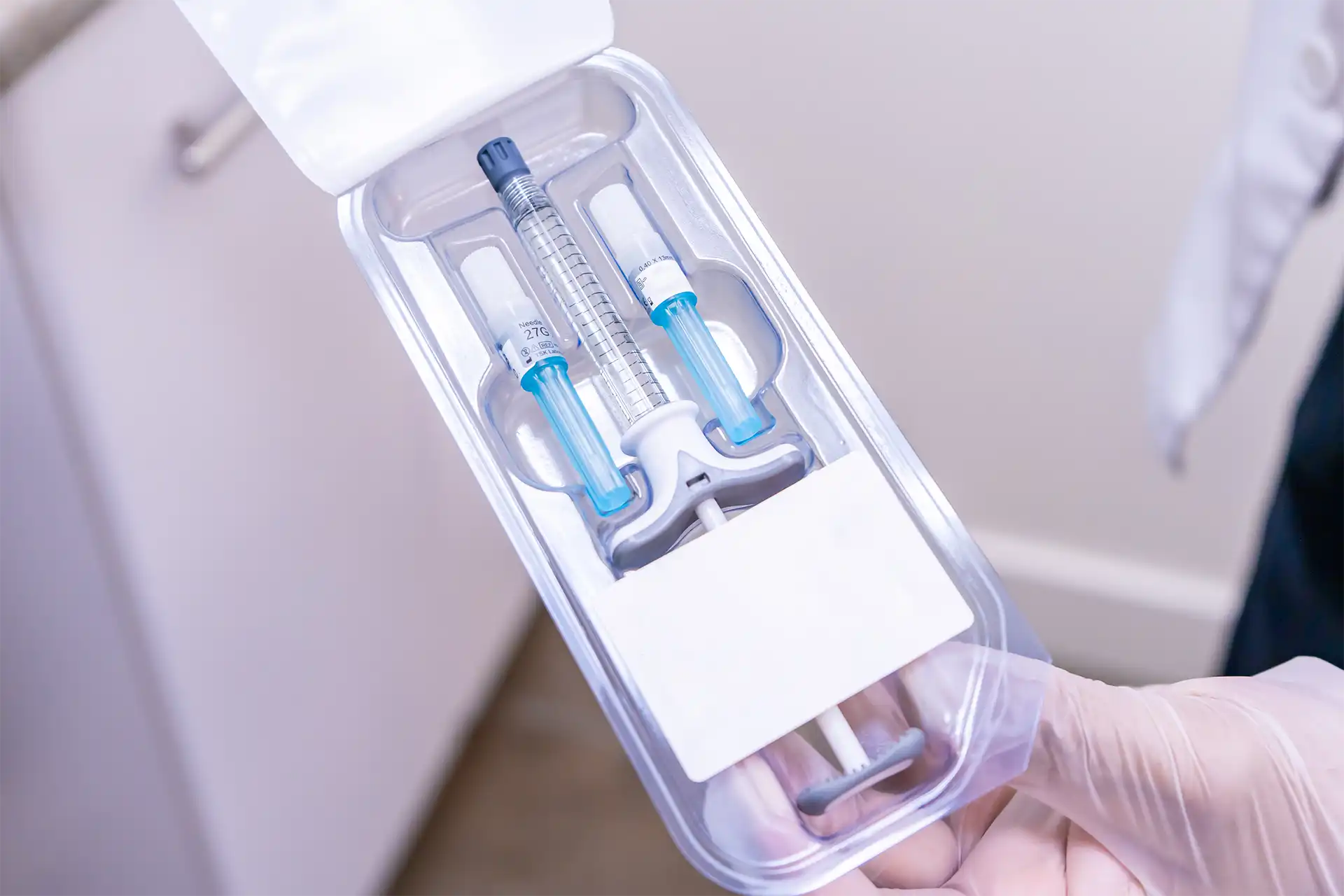 Gloved hands opening a sealed medical syringe kit inside a plastic tray package.
