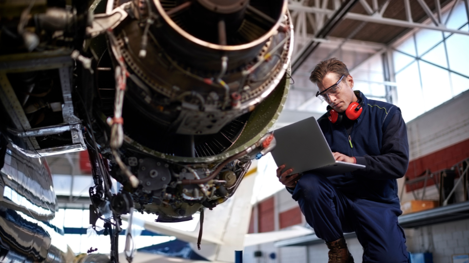 An aircraft maintenance engineer using software on a laptop to inspect and document details of an aircraft engine during routine checks.