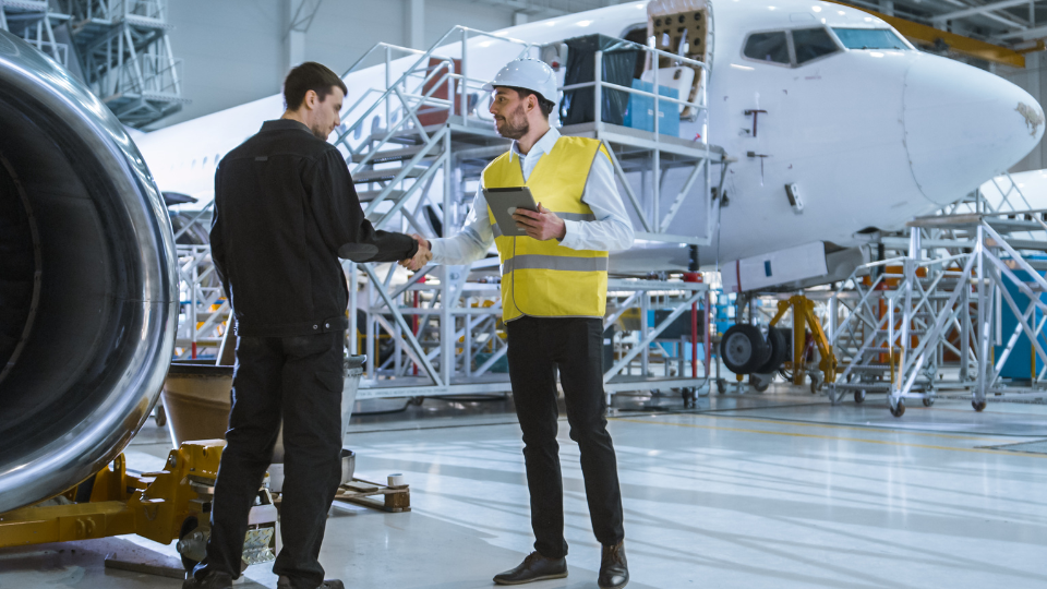 Two aviation professionals shaking hands in a maintenance hangar.
