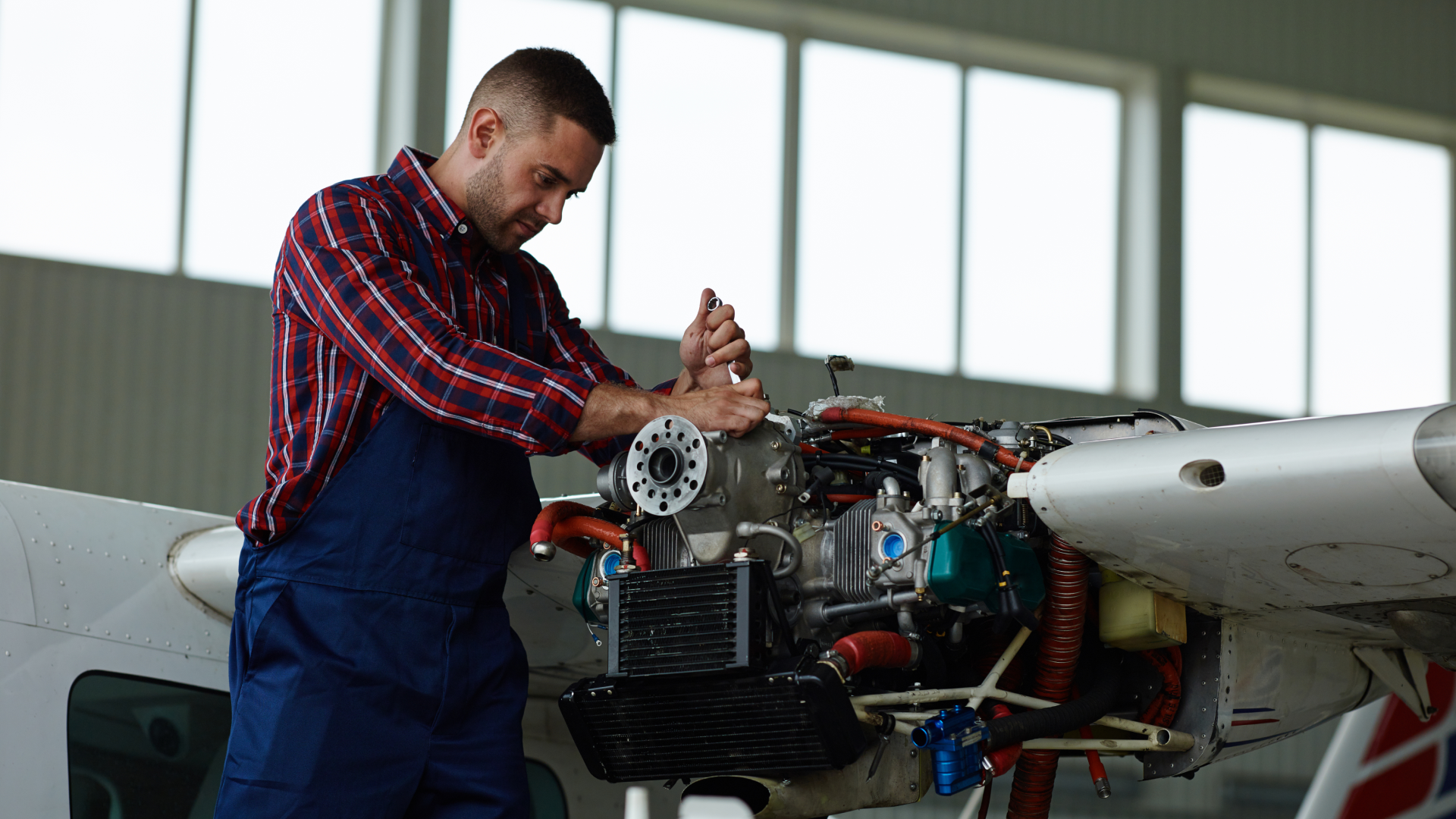 An aircraft mechanic tightening bolts on an exposed airplane engine inside a hangar during scheduled maintenance.