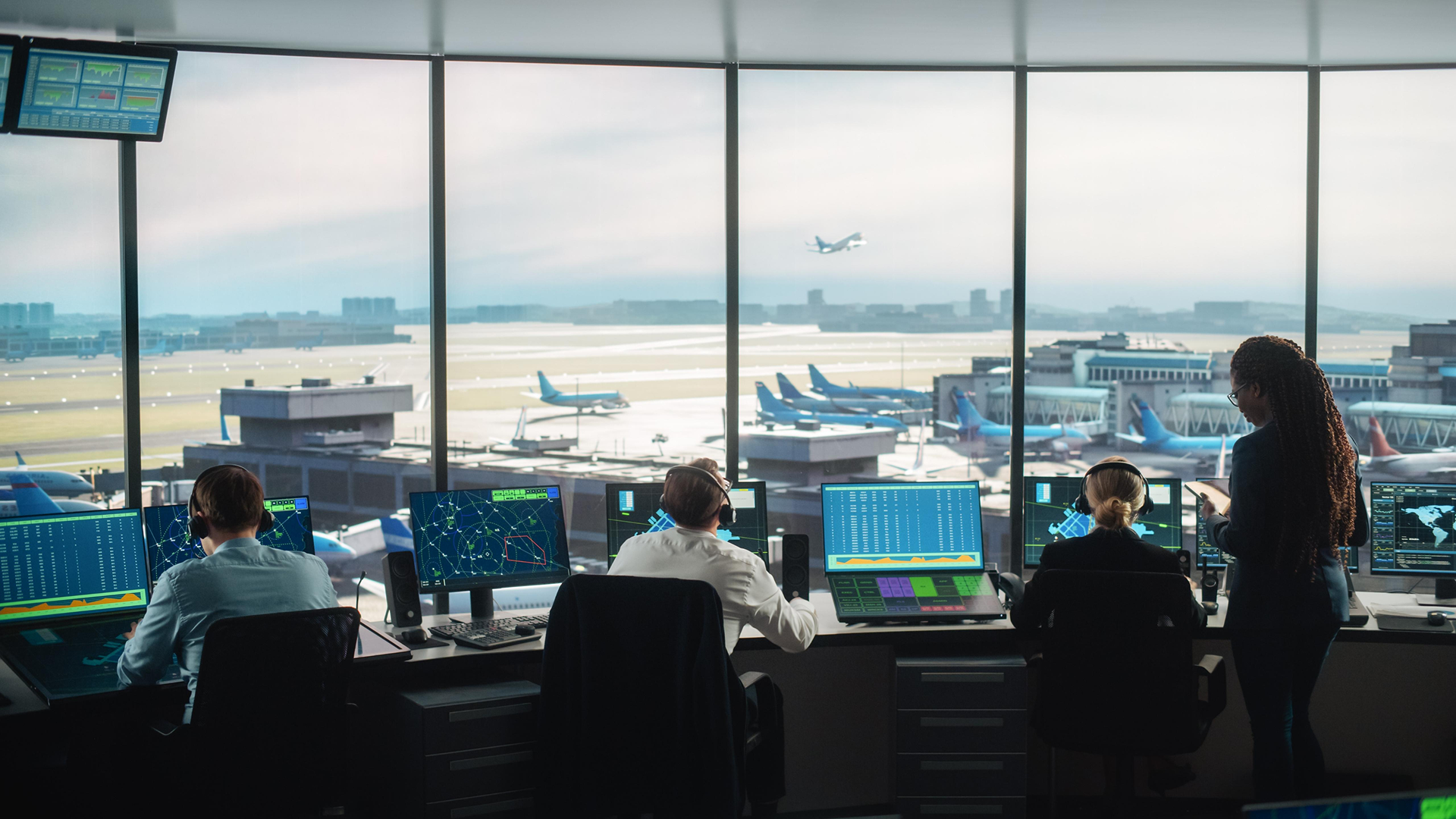 A team of air traffic controllers working in a control tower with radar screens, monitoring departing and arriving aircraft at a busy airport.