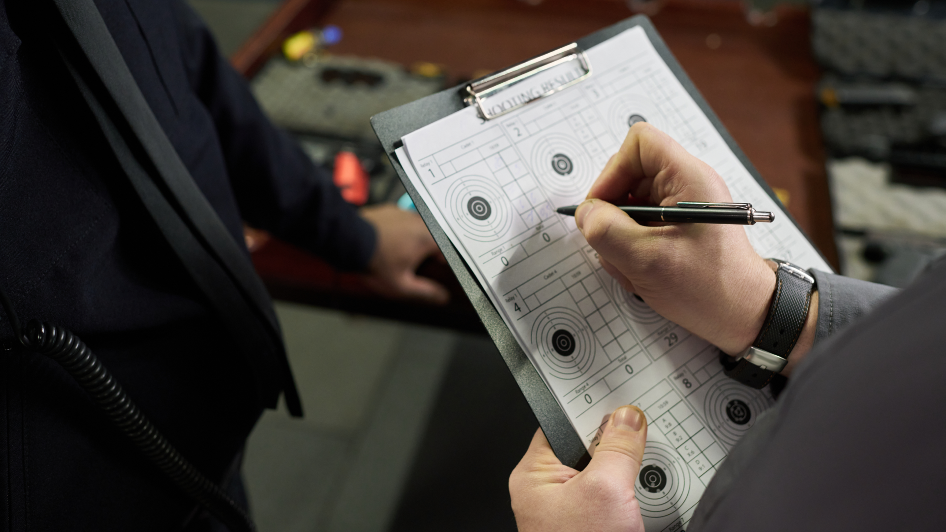 A person holding a clipboard and marking results on a target sheet with a pen.