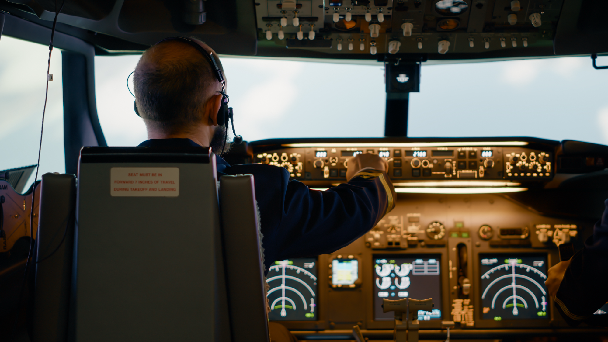 Airline pilot reviewing cockpit controls during flight operations, illustrating human factors across aviation roles.