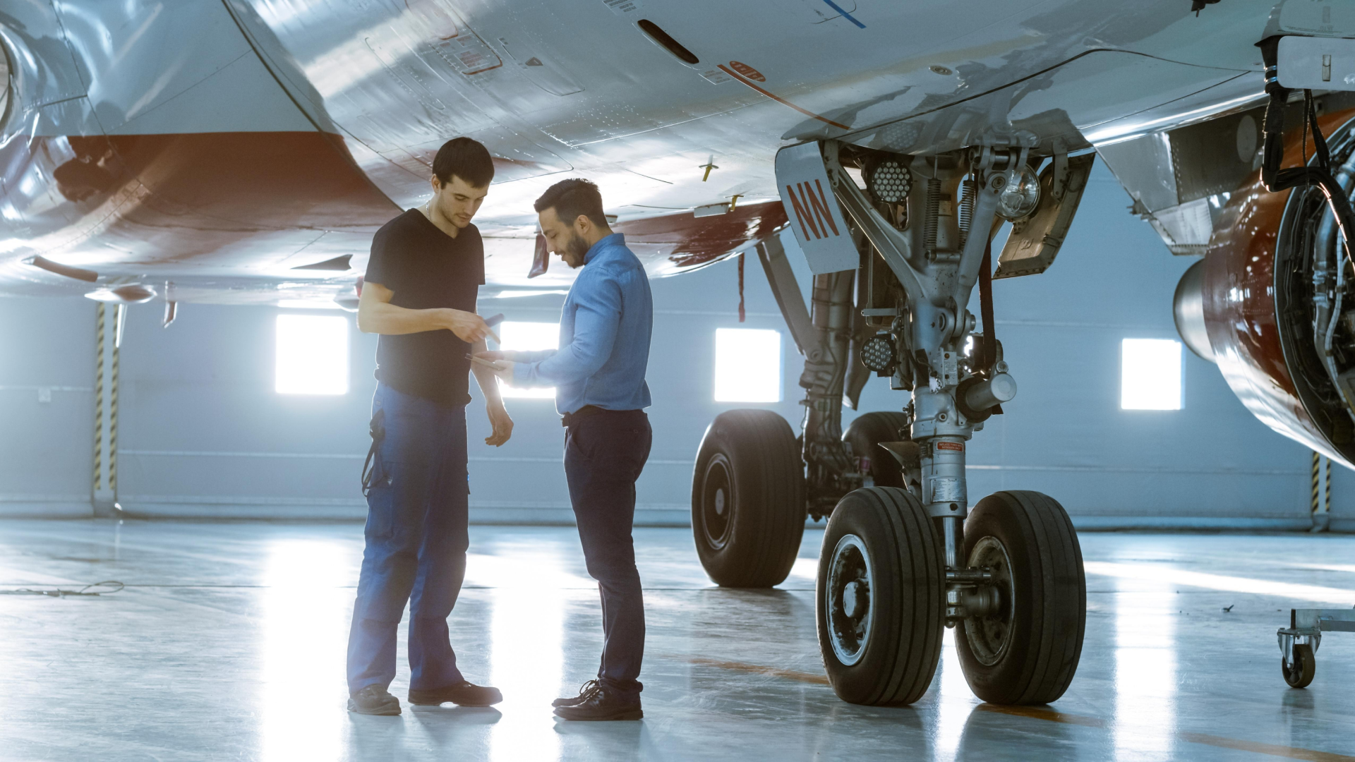 Aircraft maintenance staff reviewing data near landing gear during an aviation inspection discussion.