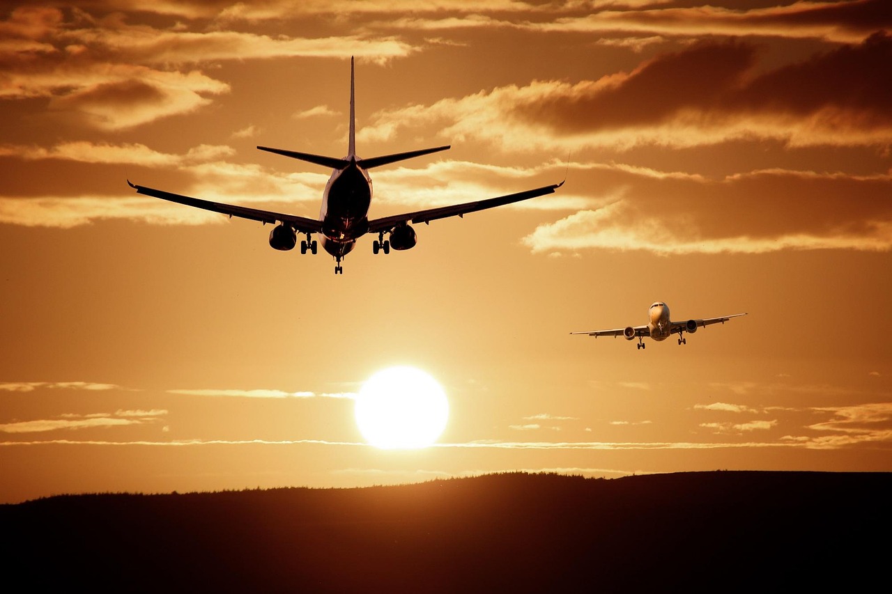 Two airplanes approach for landing against a golden sunset sky.