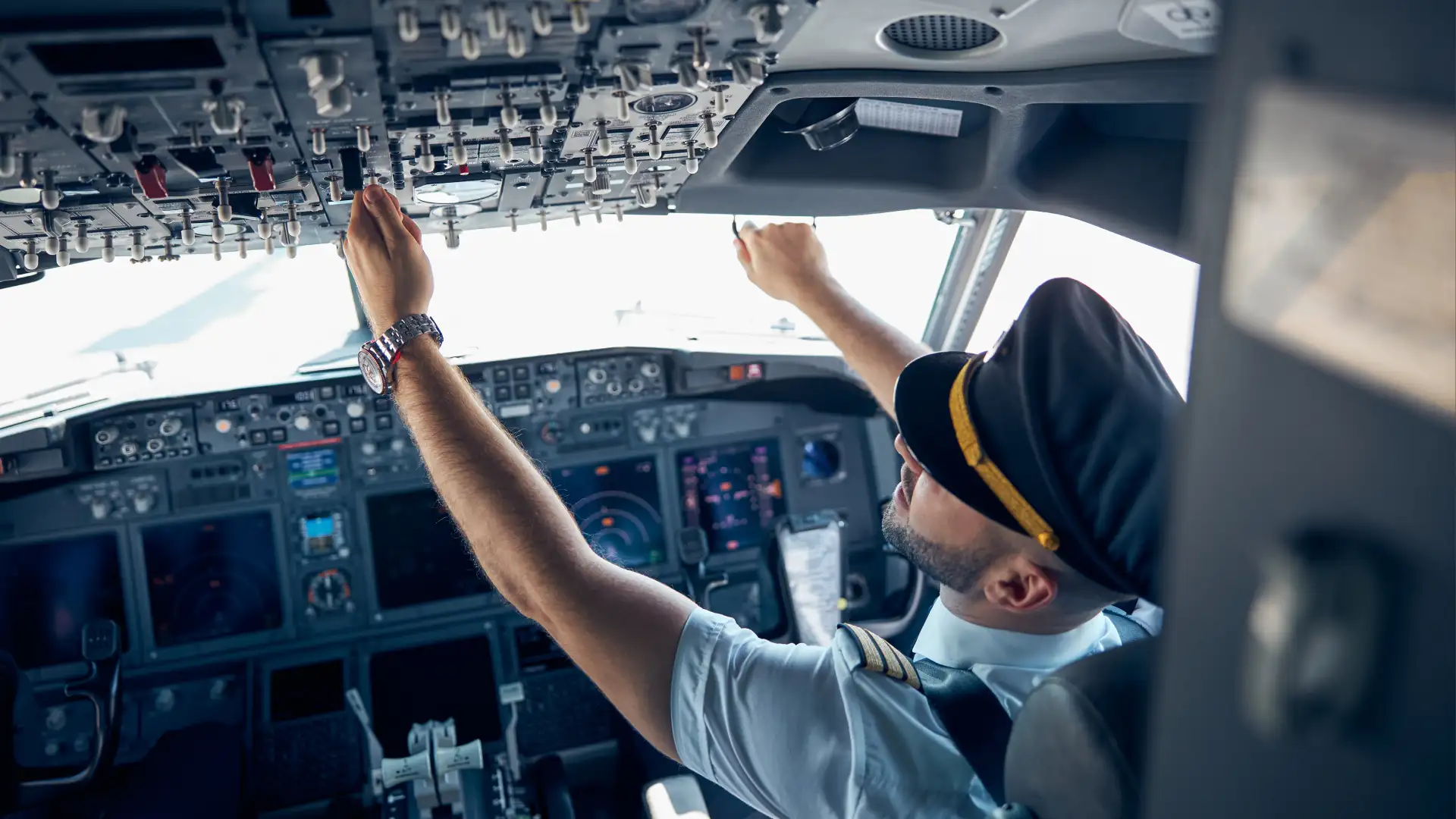 Pilot adjusting overhead cockpit switches during aircraft system checks.