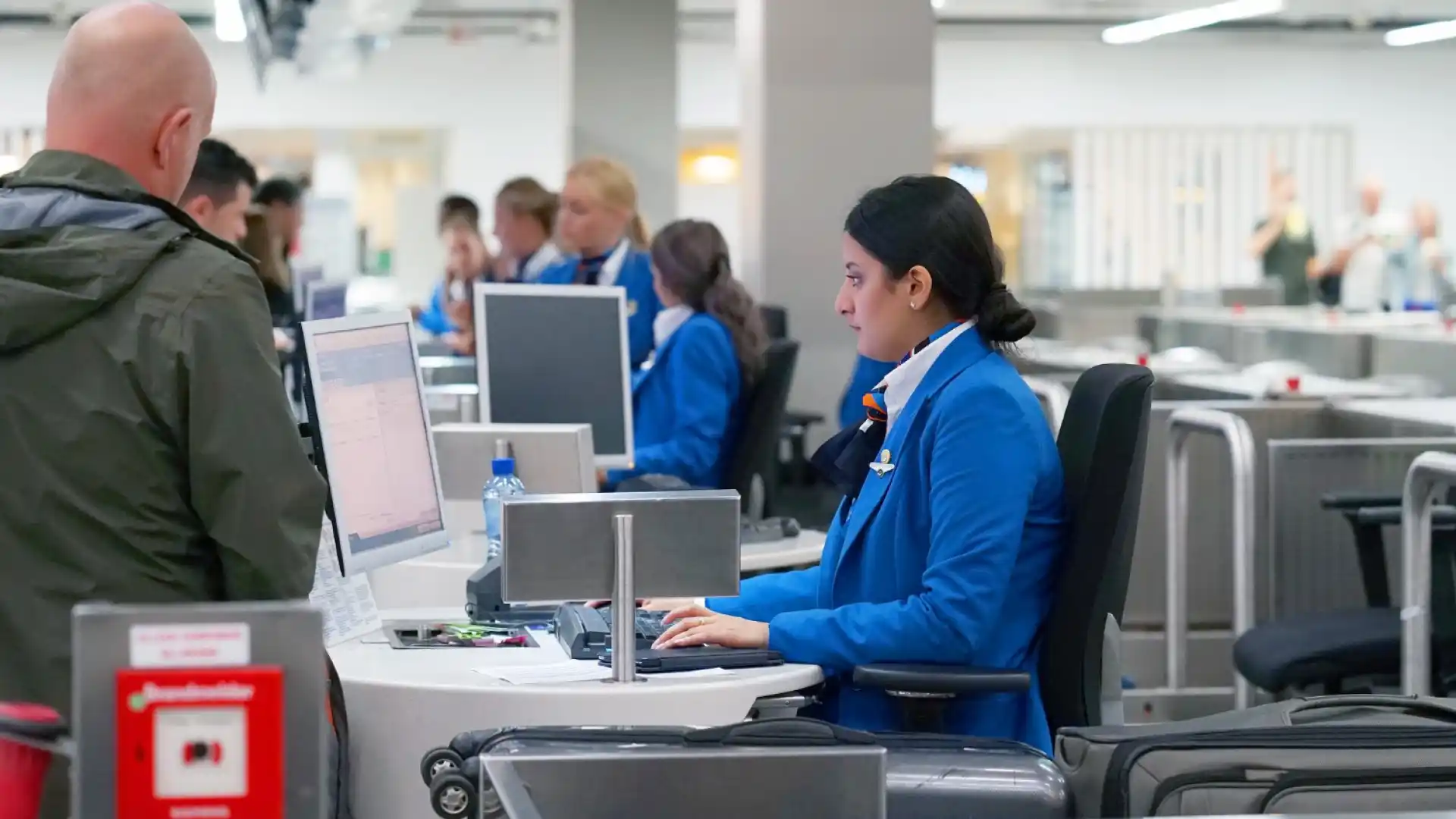 An airline employee working on a desktop computer while a person waits at the counter.