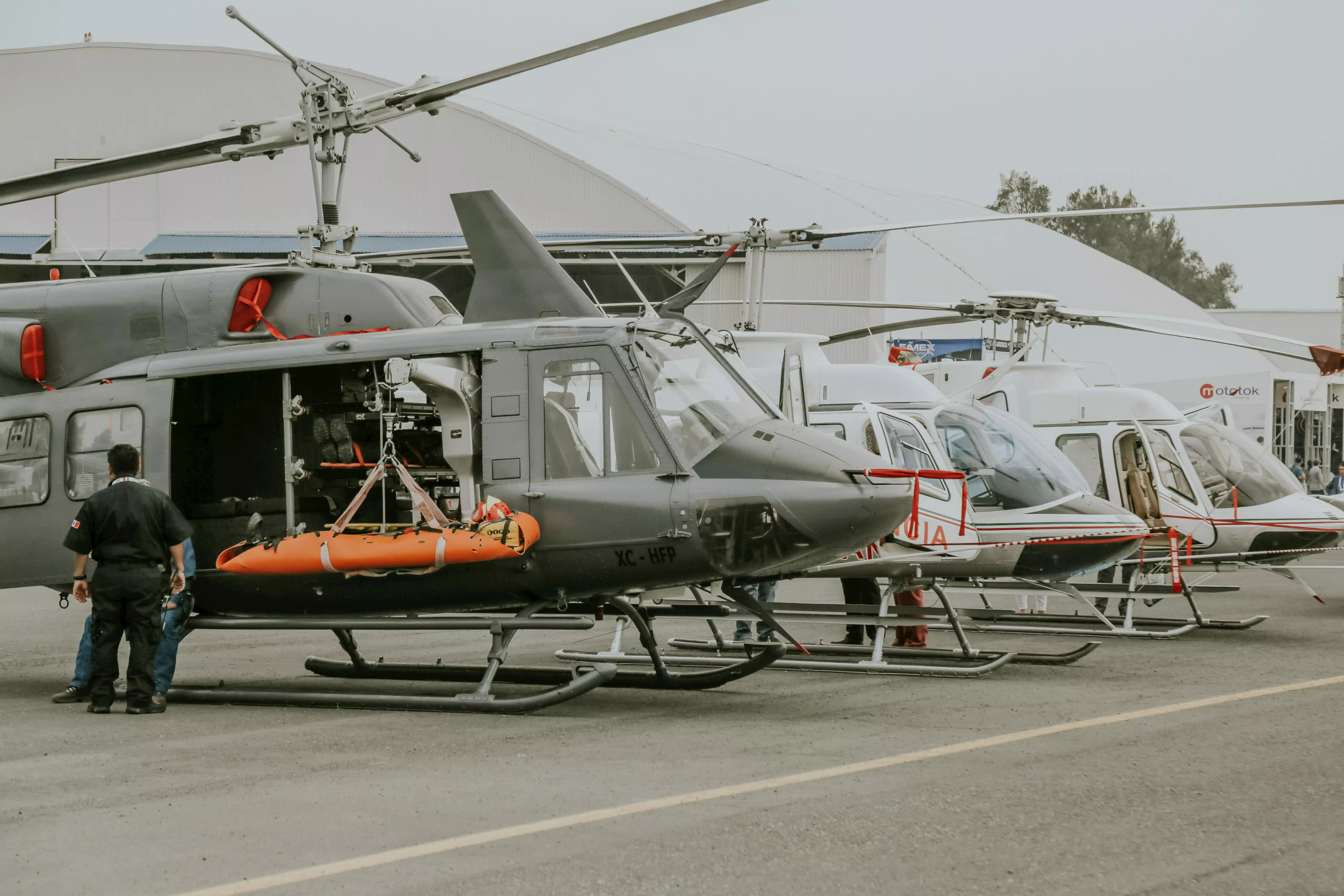 Several helicopters parked on a tarmac with one helicopter being loaded with an orange stretcher for emergency operations.