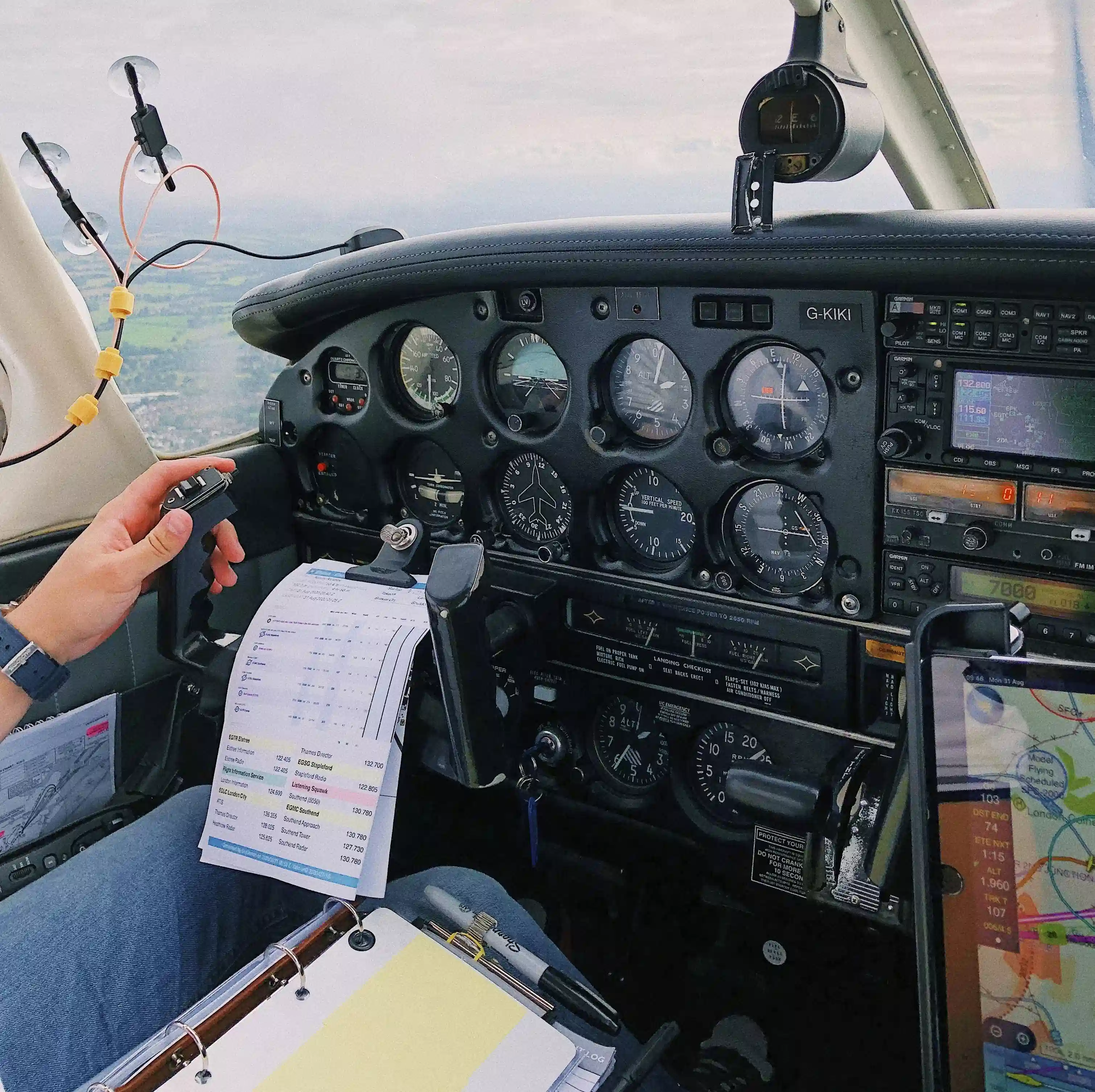 A small aircraft cockpit with a pilot holding a checklist and operating manual controls, surrounded by analogue instruments.
