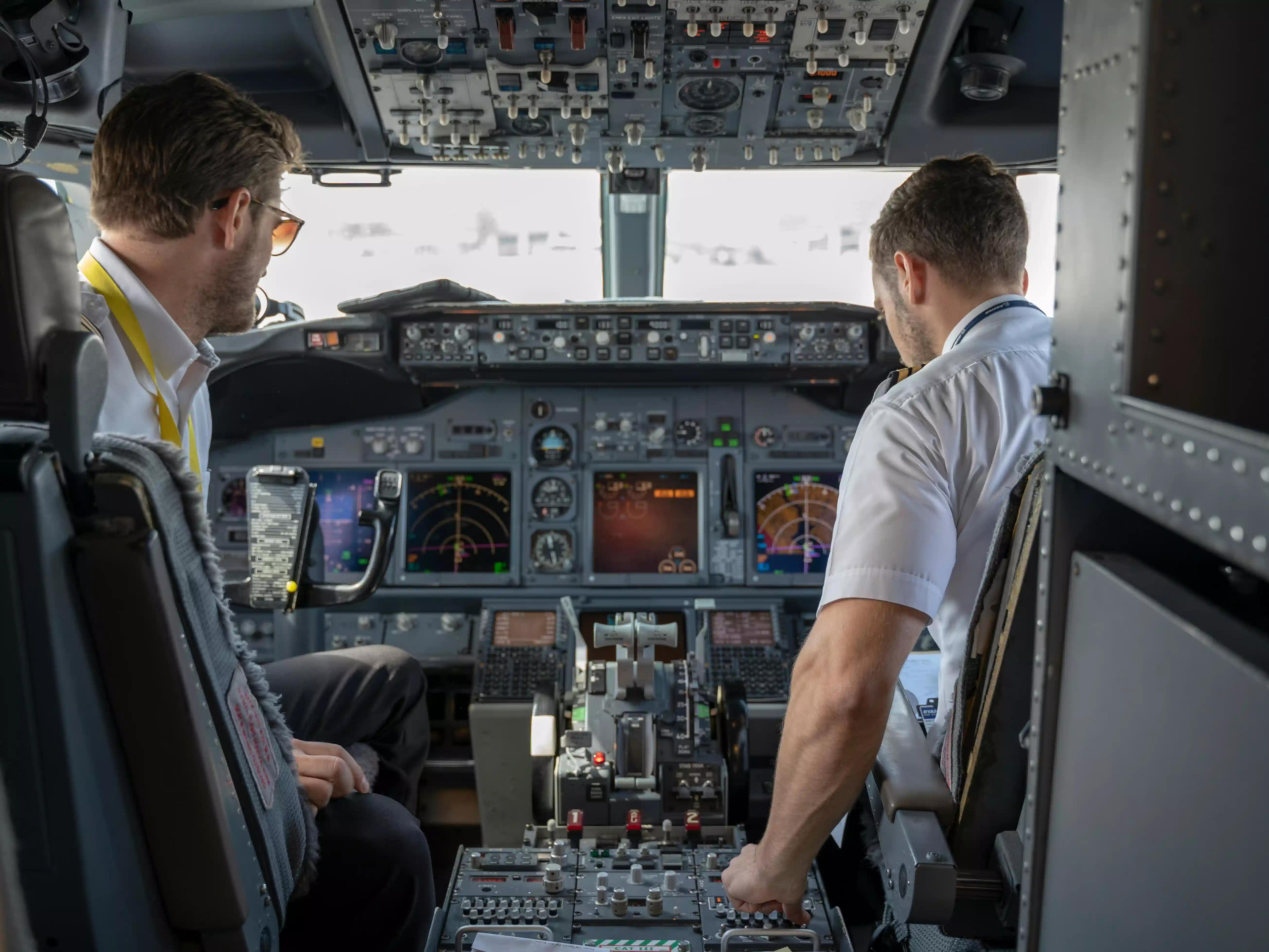 Two pilots inside an aircraft cockpit, surrounded by illuminated flight instruments and controls, actively engaged in flight management tasks while preparing for a flight.