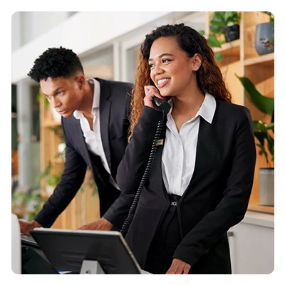 Smiling businesswoman on phone with male colleague working at computer in office.