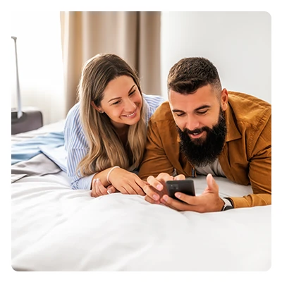 Smiling couple lying on bed looking at a smartphone screen together indoors.