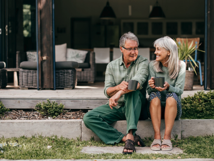 A man and woman are seated with their legs crossed, stretching their left arms up and extending them to the right side of their bodies.
