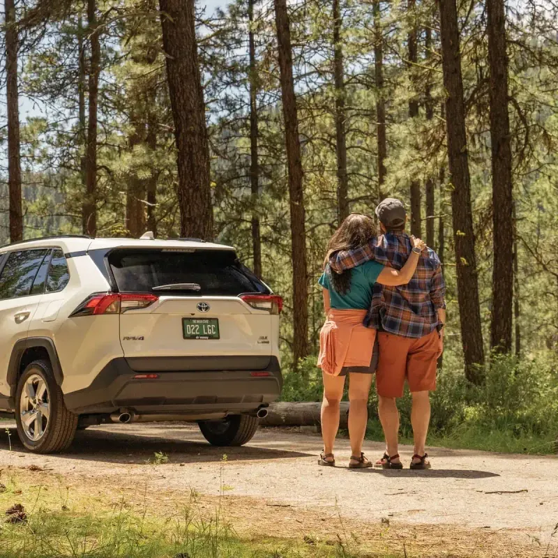 A young couple admiring the forest and trees next to their RAV4 Hybrid