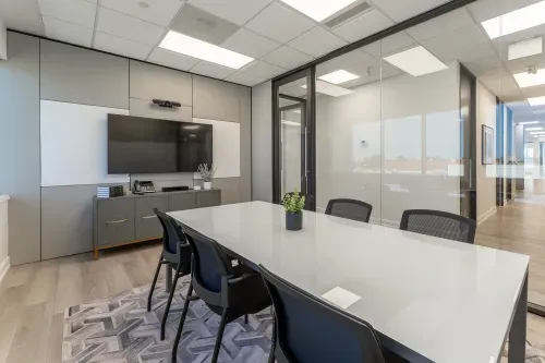 A board room with a large white marble table surrounded by contemporary office chairs. A tv is attached to the grey panned wall with a sideboard underneither.