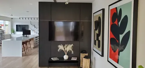 A dark grey panelled wall nook with a wall mounted tv that is above a small table with decorative accents. Brightly coloured art is mounted on the adjoining wall.
