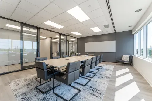 Board room with a large table surrounded by chairs. Light wood flooring with a geometric area rug.
