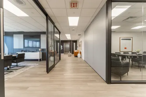 Calibrex office with a modern boardroom to the right enclosed in glass and a smaller boardroom to the right, enclosed in glass. At the back is a elevator with a cozy seating area.