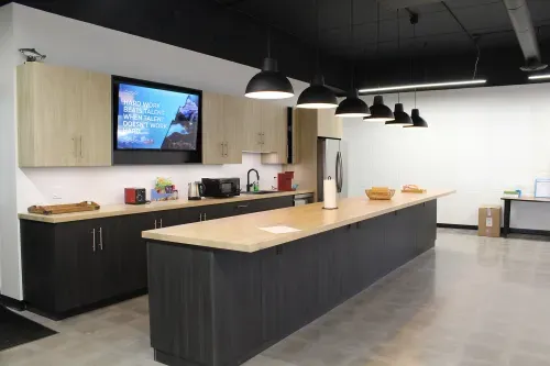 Modern kitchen with light butcher block counters, dark wood bottom cabinets and light wood upper cabinets. 6 black pendant lights light up a large island.