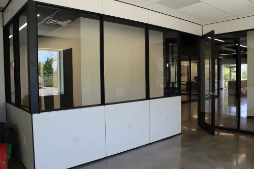 Inside an office looking into the hallways. The walls are glass on top an white paneling on the bottom.