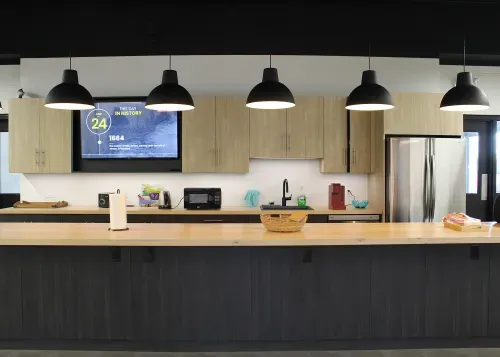 Modern kitchen with light butcher block counters, dark wood bottom cabinets and light wood upper cabinets. 6 black pendant lights light up a large island.