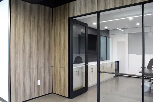 A doorway into an office that has light wood panelling on the walls and glass and black metal windows.