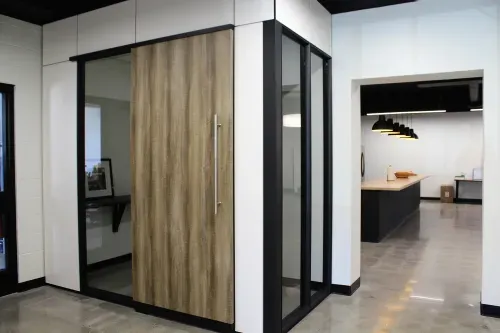 A small corner office with wood panelling, glass and black metal windows and white walls.