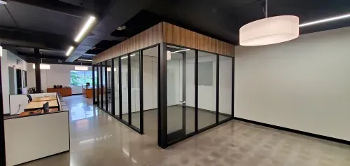 A large open office space with a pod of offices in the middle of the room seperated by glass walls. The floors are shiny grey concrete, the ceilings are black with modern lighting.
