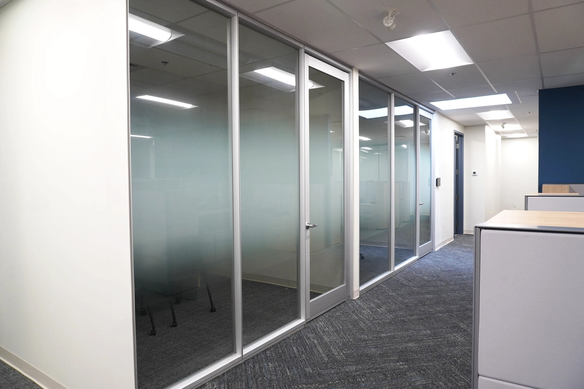 Corporate office space with hallway with frosted glass windows and doors leading into meeting rooms and offices