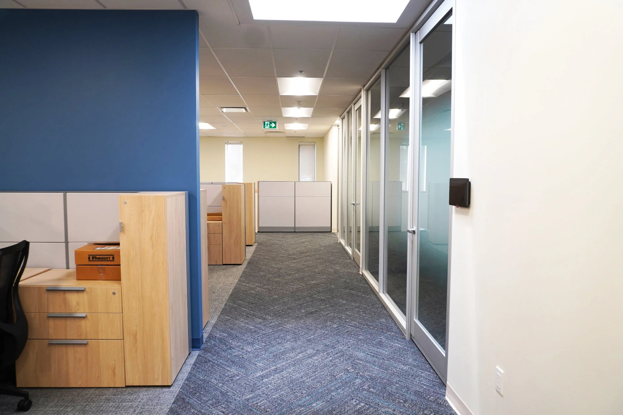 Main floor space in office with desks and chairs, frosted glass windows and doors leading to more offices line wall