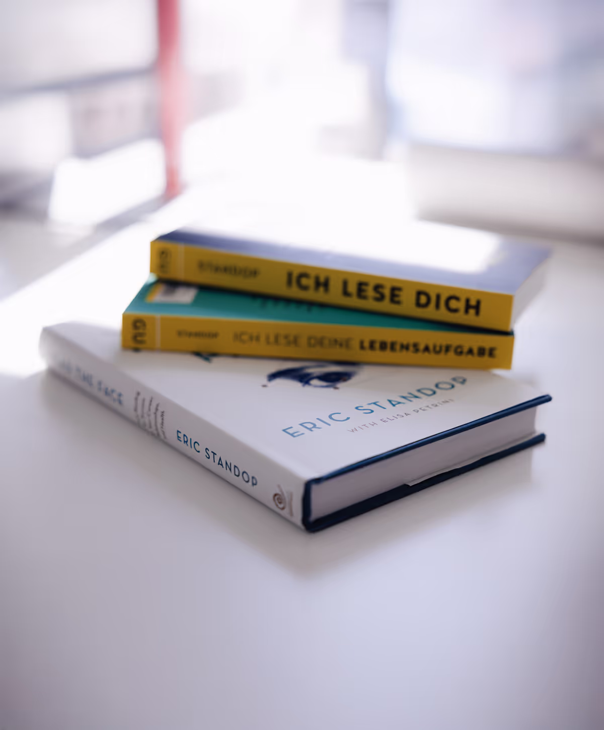 Drei übereinanderliegende Bücher auf einem weißen Tisch, zwei mit gelbem Umschlag und ein drittes von Eric Standop.