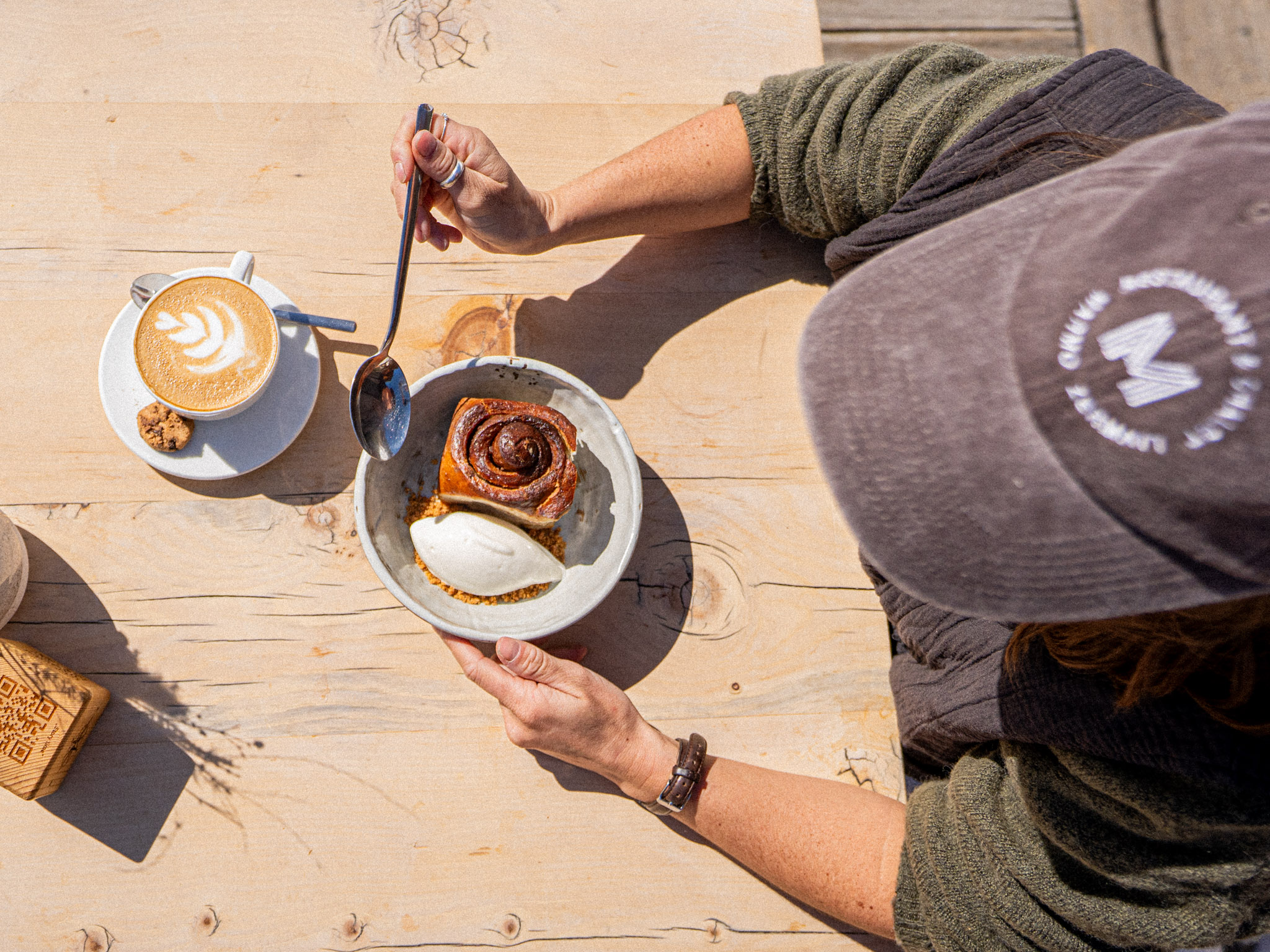 Gast geniesst Zimtknoten mit Fior di Latte und Cappuccino auf der sonnigen Terrasse des MARMO, Furi Zermatt