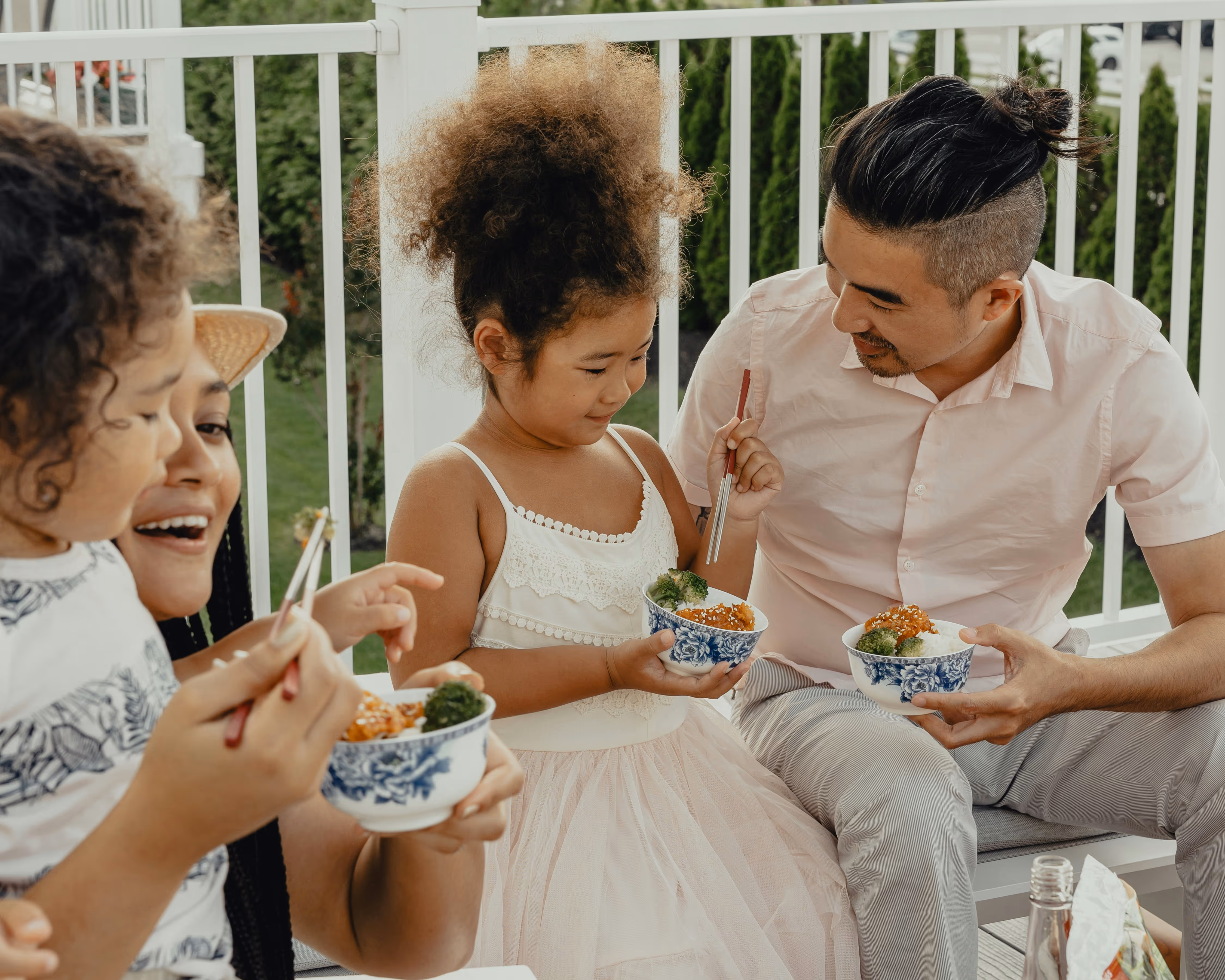 Family of mixed heritage sharing a meal together on a porch, smiling warmly