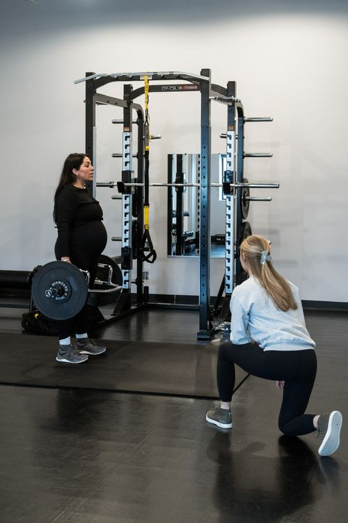 Photo of Shelby watching the form and technique of a pregnant woman doing deadlifts.